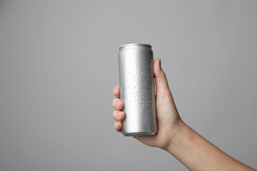 Canvas Print - Woman holding aluminum can with beverage on grey background, closeup. Space for design