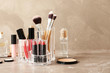Lipstick holder with different makeup products on table against color background. Space for text