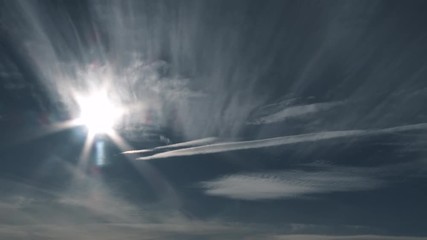 Wall Mural - Sun shining against wide open blue sky with various clouds passing by.