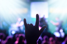 Silhouette Of A Male Hand Showing Rock Gesture Against Blurred Stage With Rock Players During Performance