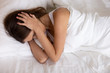 © fizkes - Young annoyed woman lying in bed holding head in hands feeling strong headache migraine suffering from insomnia noise irritated by noisy neighbors covering ears can not sleep, hangover, top view