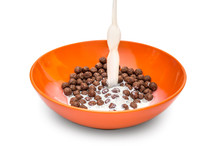 Milk pouring into the bowl with chocolate cereal balls on white background.