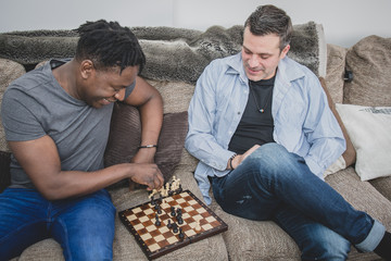 Wall Mural - A gay couple enjoying time indoors at home, playing chess. 