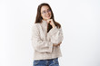 © Cookie Studio - Waist-up shot of happy charismatic young brunette in glasses and warm sweater tilting head and smiling holding hand on chin, crossing arm against chest having conversation over gray background
