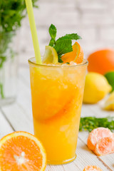 Juiced cocktail in glass and fresh fruits with leaves on white wooden background, orange, lemon and lime vitamin drink or cocktail. Closeup.