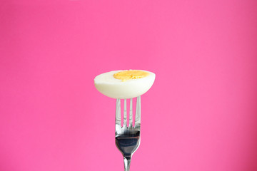 Wall Mural - Half boiled egg on a pink background. Food on fork