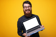 © Vulp - Happy man in gray shirt showing laptop computer screen at the camera over yellow background