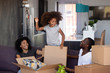 Happy child girl jump out of box play with parents in living room, excited joyful african family and kid daughter laugh having fun packing unpacking boxes, black family moving in new home relocation