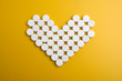 Pills in shape of heart on yellow background. Flat lay, top view.