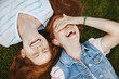 Friendship is miracle. Joyful and carefree cute redhead girls with freckles, lying on green grass and laughing out loud, woman covering eyes while chuckling, fooling around and having fun