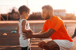 Trainer encouraging little sporty boy to play football. Summertime in the morning.