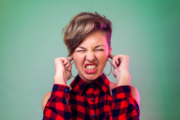 People and emotions - a portrait of smiling young woman with short dark hair closes ears with fingers