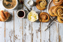Variety Of Homemade Puff Pastry Buns Cinnamon Rolls And Croissant Served With Coffee Cup, Jam, Butter As Breakfast Over White Plank Wooden Background. Flat Lay, Space