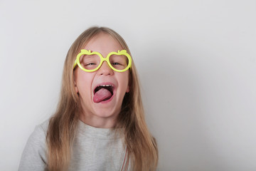  Portrait of funny naughty little girl in glasses making faces at camera, shows tongue. Expressive facial expressions . Human emotions, reactions, feelings and attitude .