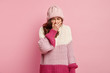 © WHstudio Leushin N - Negative human feelings, emotions concept. Dejected upset woman keeps palm on mouth, feels upset, cries from despair, wears casual headgear and warm knitted sweater, isolated on pink background