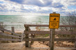 Rip Current Warning. Sign at beach entrance warning of dangerous rip currents as waves crash on to the coast of Lake Michigan.