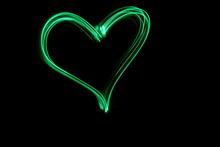 Long Exposure, Light Painting Photography.  Vibrant Neon Green Heart Symbol Shape, Love And Romance Concept, Against A Black Background