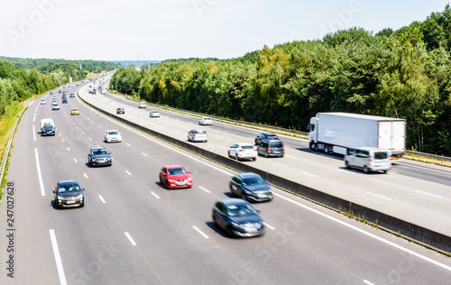 Fotomural Heavy but fluid traffic on the eight-lane A10 highway in France in the direction of Paris by a hot summer day with cars, vans, trailers and semitrailer truck driving