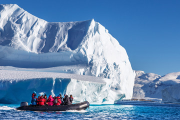 tourists sitting on zodiac boat, exploring huge icebergs driftin