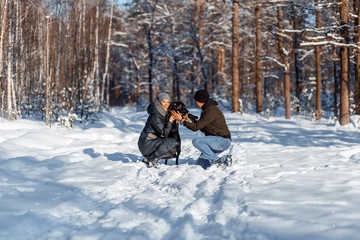 Wall Mural - A happy couple with a dog (black Labrador) having fun outside in the forest on a sunny frosty winer day.