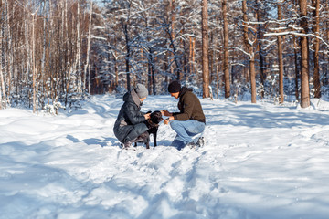 Wall Mural - A happy couple with a dog (black Labrador) having fun outside in the forest on a sunny frosty winer day.