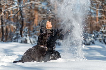 Wall Mural - A happy woman with a dog (black Labrador) having fun outside in the forest on a sunny frosty winer day.