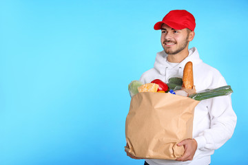 Sticker - Food delivery courier holding paper bag with products on color background. Space for text