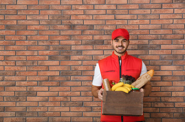 Sticker - Food delivery courier holding wooden crate with products near brick wall. Space for text