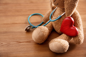 Wall Mural - Toy bunny, stethoscope and heart on wooden background, closeup. Children's doctor