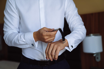 Wall Mural - Close-up man puts on a gold watch with a leather belt, businessman is dressed in a stylish suit, a white shirt.