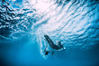 Surfer girl with surfboard dive underwater under ocean wave.
