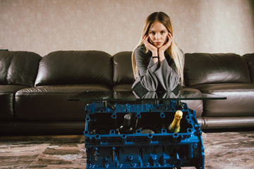 Wall Mural - Young caucasian blonde girl sitting on sofa at luxury interior with custom v8  car engine table. Fashion picture and beautiful smile