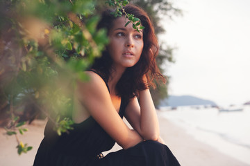 Wall Mural - portrait of a beautiful young woman with dark hair in a frame of branches and green leaves, on the c