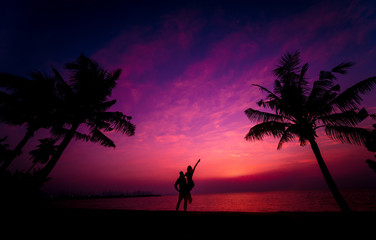 Silhouette of couple on tropical beach during sunset on background of palms and sea