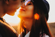 © Strelciuc - Side view portrait of a lovely young girl with eyeglasses and hat trying to kiss her boyfriend with closed eyes against sunset.