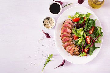 Japanese traditional salad with pieces of medium-rare grilled Ahi tuna and sesame with fresh vegetable salad on a plate. Authentic Japanese food. Top view. Copy space.