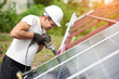 © anatoliy_gleb - Profile view of technician connecting blue shiny solar photo voltaic panel to metal platform using electrical screwdriver on warm summer day. Stand-alone solar panel system installation concept.