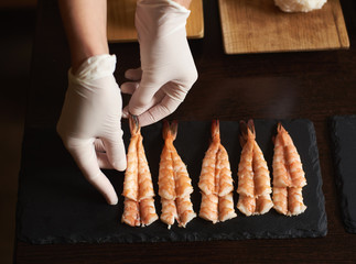 Closeup view of woman's hands in gloves are preparing shrimp for rolling sushi in restaurant