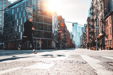 Young athlete running through the New York streets. Sporty man fast running early morning in sunny day through urban city