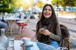 © moofushi - Portrait einer jungen, attraktiven Frau mit ihrem Telefon draussen in einem Cafe