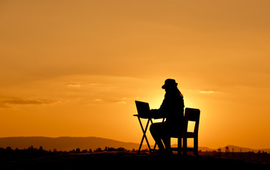 Wall Mural - silhouette a beautiful woman is working on a notebook at sunset.