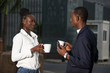 © vystekimages - Two coworkers drinking coffee near the office building outside i