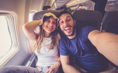 young handsome couple taking a selfie on the airplane during flight around the world. they are a man