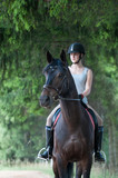 Fototapeta Konie - Portrait of black horse with teenage girl equestrian on it