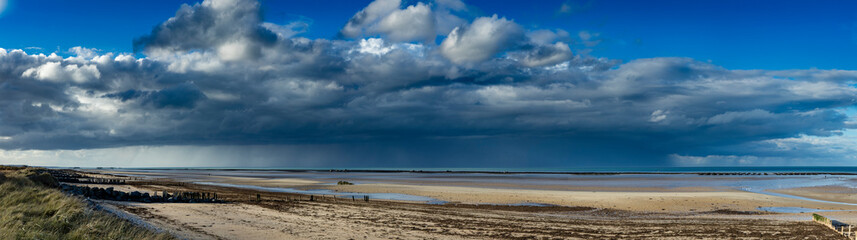 the normandy beaches in france showing ruins and relics from world war II on golden sands and dark blue waters