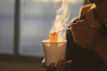 Man hand holding plastic fork of instant noodles with smoke rising in the home sunset background, Sodium diet high risk kidney failure, Healthy eating concept