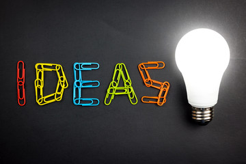 Colorful ideas word or text next to a light bulb isolated on black background