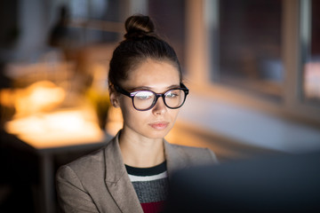 Poster - Young casual businesswoman in eyeglasses concentrating on working in front of computer monitor in office