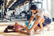 © Dusan Petkovic - Bearded personal trainer helping woman to stretch arms. Woman lying on mat, gym interior.
