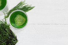 Wheatgrass Fresh Juice And  Green Wheatgrass Plants Isolated On White Wooden Background, Copy Space On The Right Side 